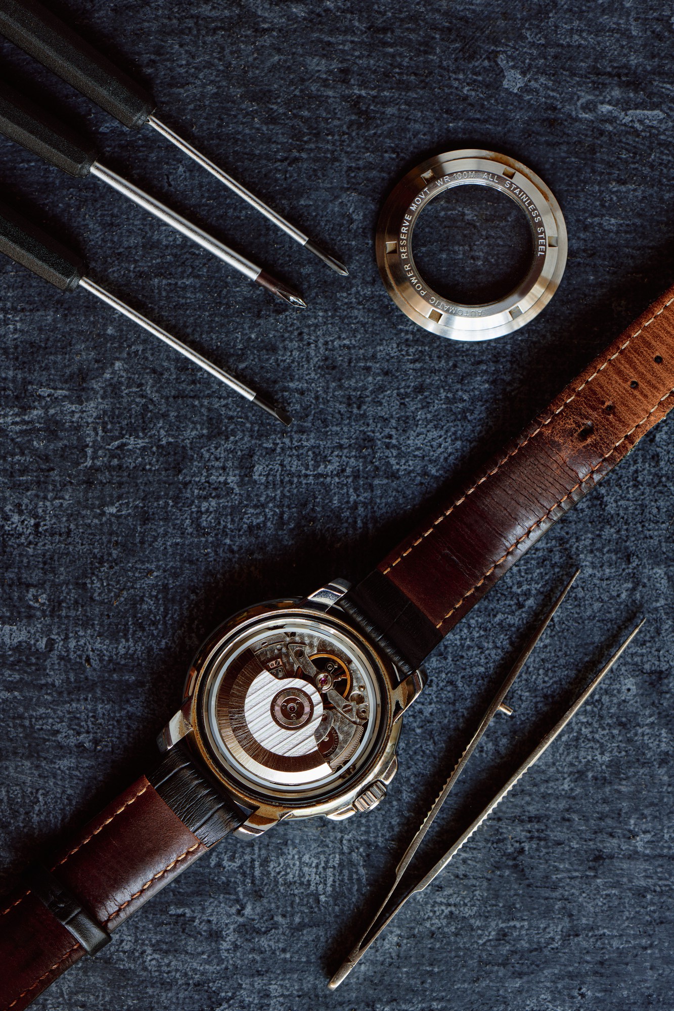 Orologio con cinturino in pelle, cacciaviti e ghiera del fondello su un piano da banco